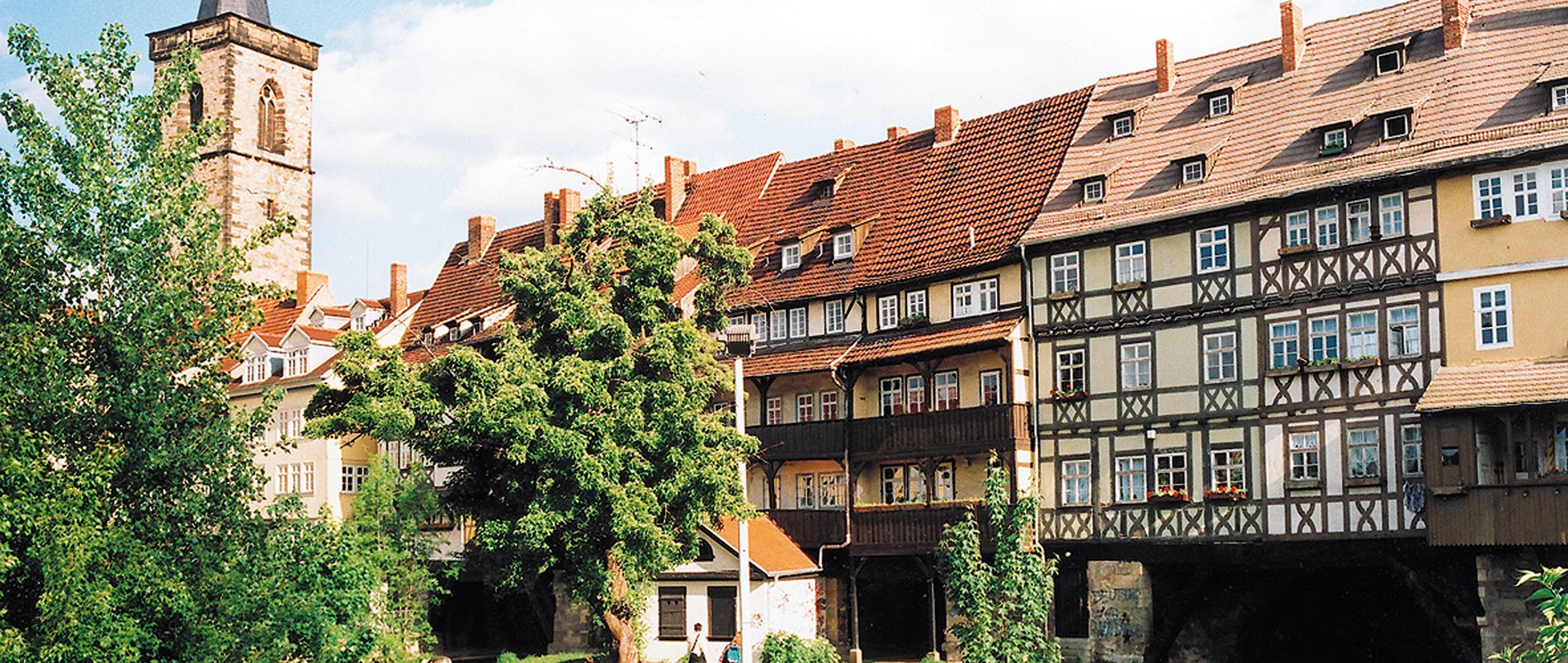 Blick auf die Krämerbrücke in Erfurt mit Fachwerkhäusern und einem Kirchturm im Hintergrund.