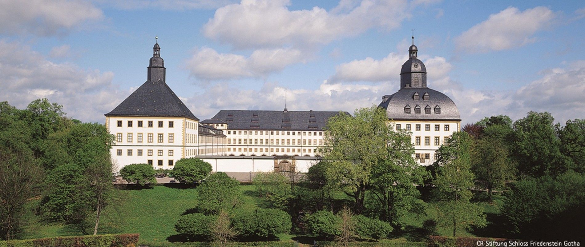 Schloss im barocken Stil mit zwei großen Kuppeltürmen, umgeben von gepflegten Gärten.