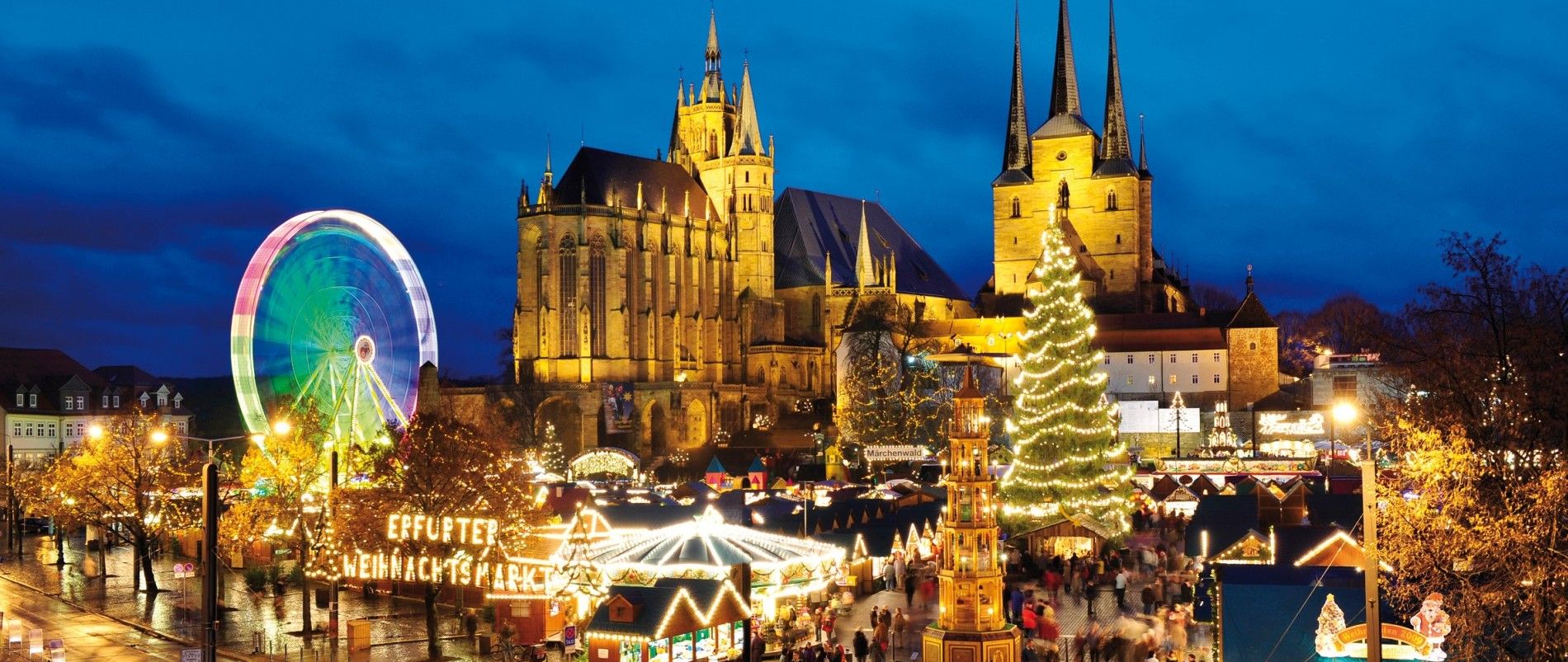 Beleuchteter Weihnachtsmarkt mit Riesenrad und Kirche.