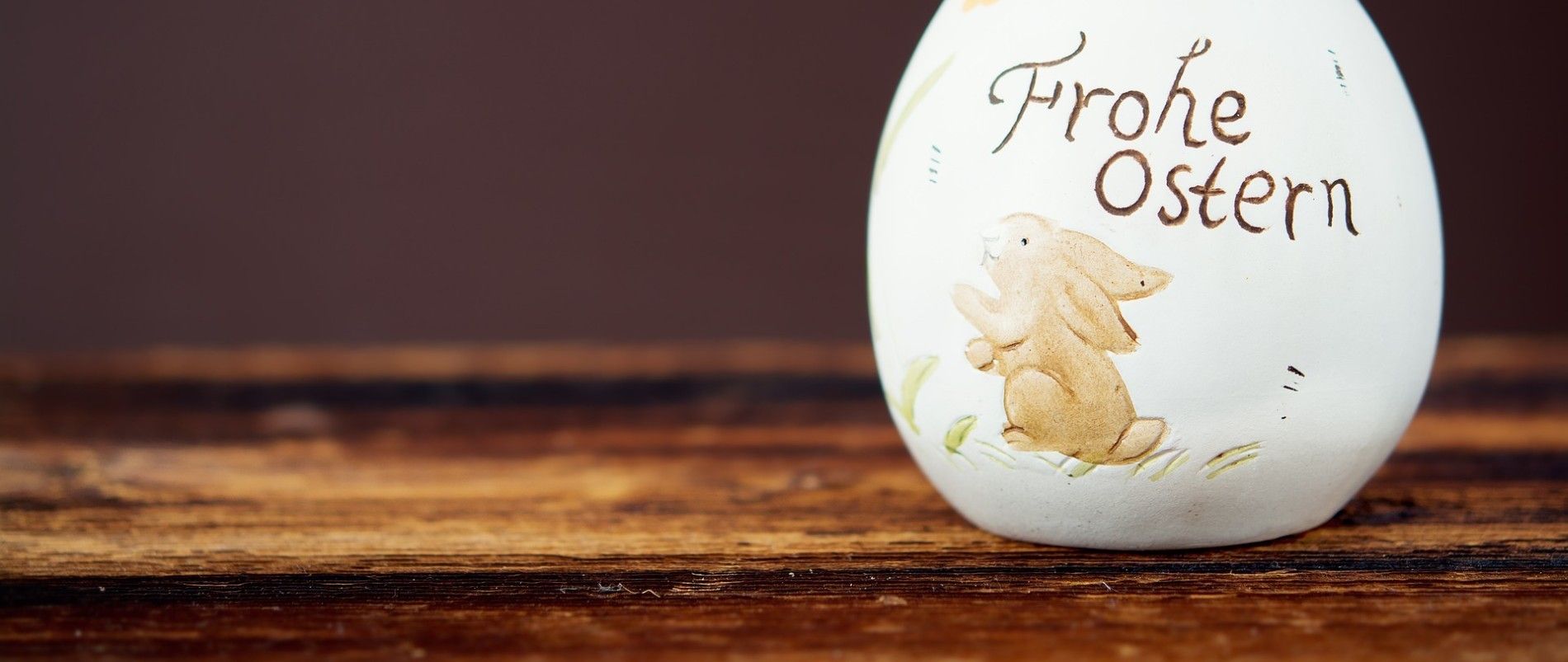 Ein dekoratives Osterei mit einem aufgemalten Hasen und der Aufschrift 'Frohe Ostern' auf einem Holztisch.
