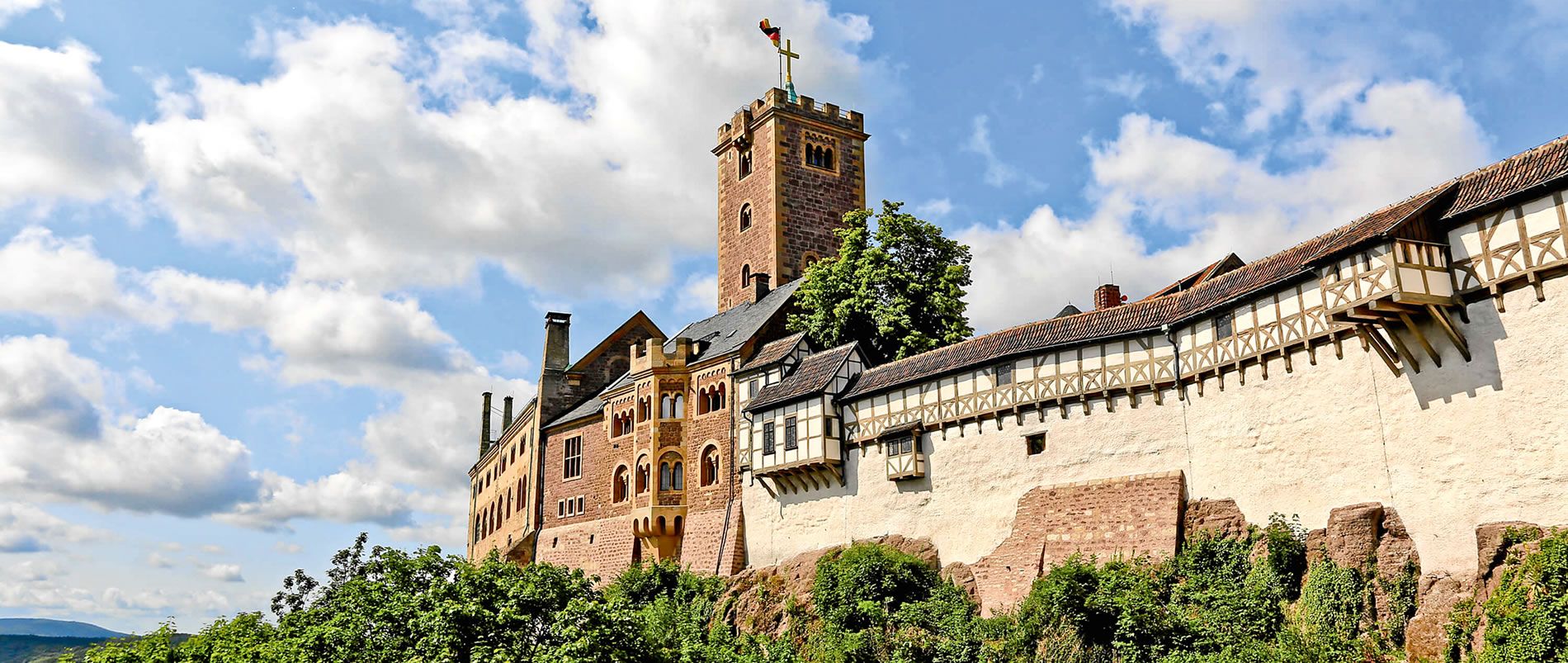Blick auf eine große historische Burg auf einem Hügel unter einem blauen Himmel mit weißen Wolken.
