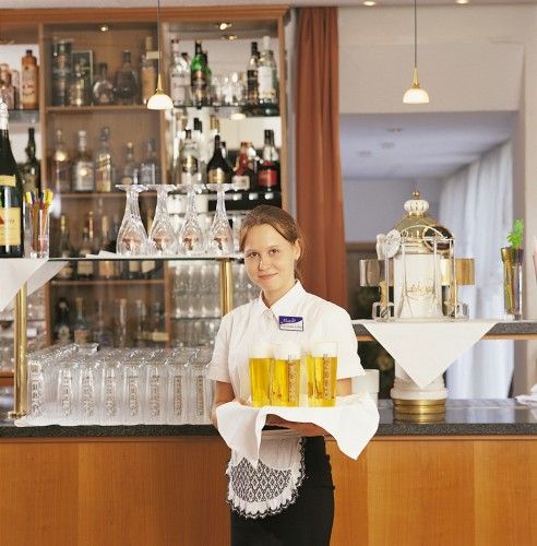 Kellnerin in einem Restaurant mit einem Tablett voller Getränke vor einer Bar mit Spirituosen.