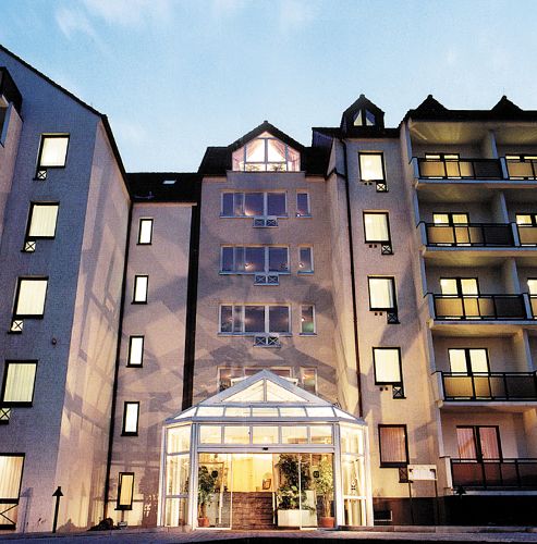 Mehrstöckiges Gebäude mit beleuchteten Fenstern und gläsernem Eingang bei Dämmerung.