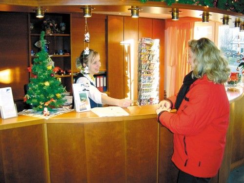 Eine Frau in roter Jacke steht am Empfang eines Hotels, dekoriert mit Weihnachtsbaum.