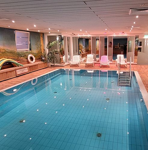 Kleines Hallenbad mit Liegestühlen und Dekorationspflanzen.