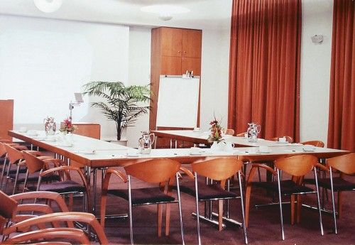 Leerer Konferenzraum mit U-förmiger Tischanordnung, Stühlen, einem Flipchart und Pflanzen.