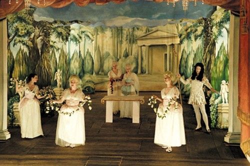 Theaterszene mit Figuren in historischen Kostümen in einem bewaldeten und klassischen Dekor.