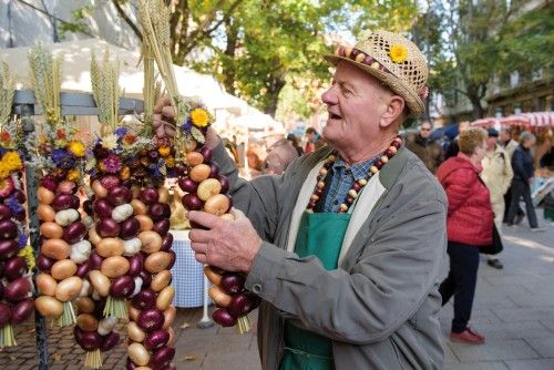 Mann auf einem Markt hält eine Kette aus bunten Zwiebeln und Trockenblumen.