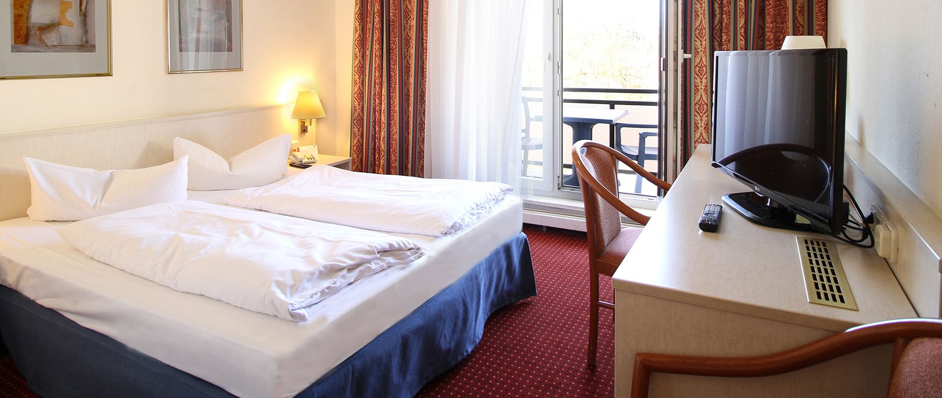 Hotelzimmer mit Doppelbett, Vorhängen, Schreibtisch, Stuhl und Fernseher.